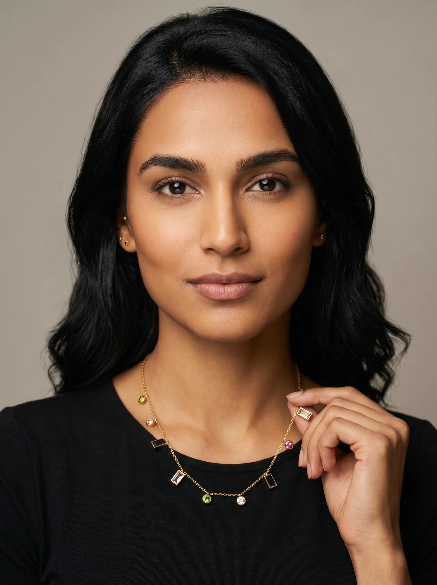 Aurum & Isle Mosaic charm necklace in gold with scattered gemstone charms, worn with black top.