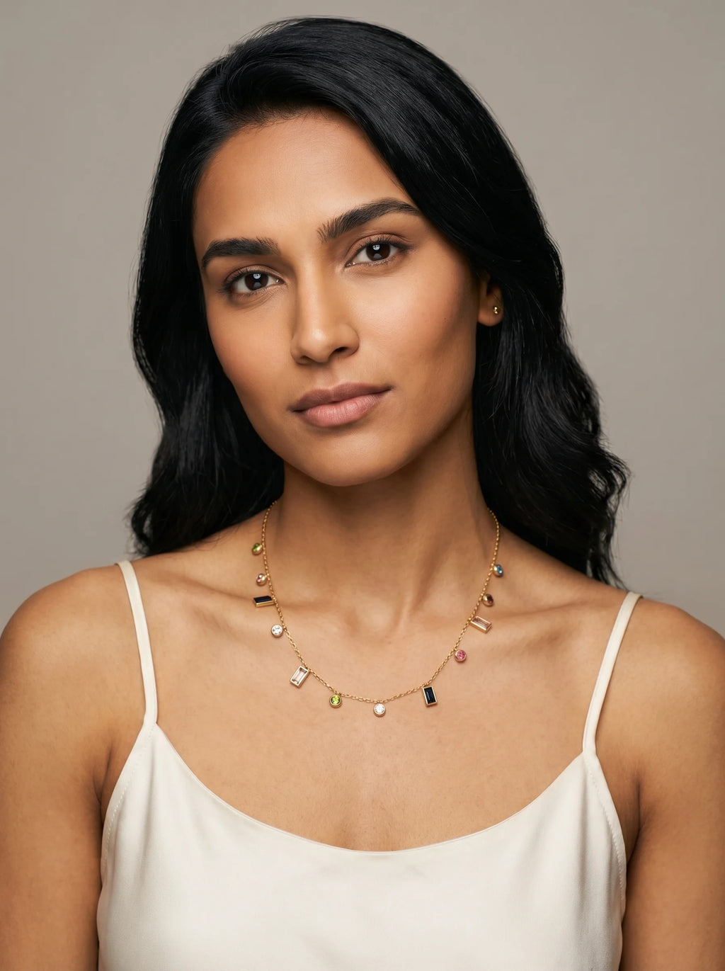 Model wearing Aurum & Isle Mosaic gold charm necklace with coloured stones, paired with cream slip dress.