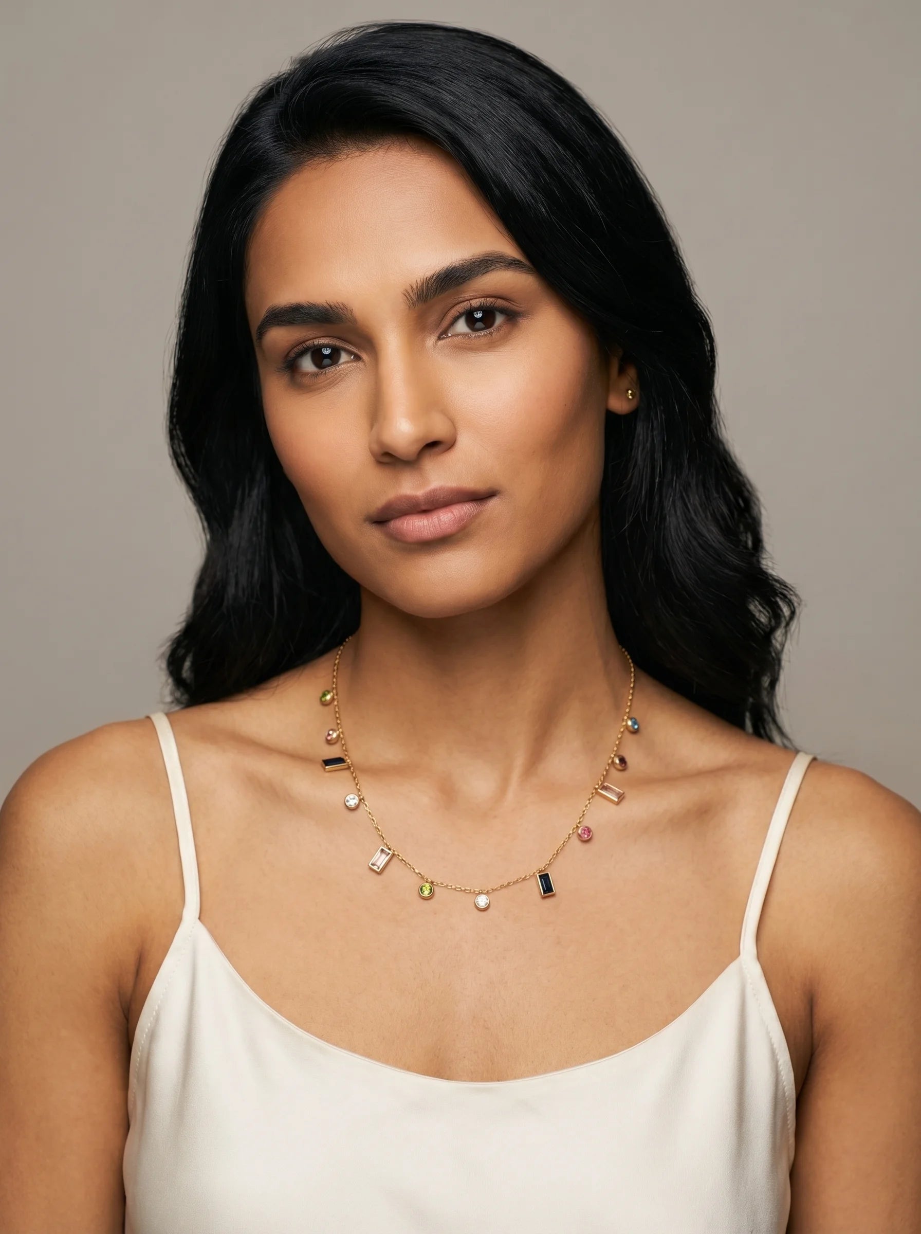 Model wearing Aurum & Isle Mosaic gold charm necklace with coloured stones, paired with cream slip dress.