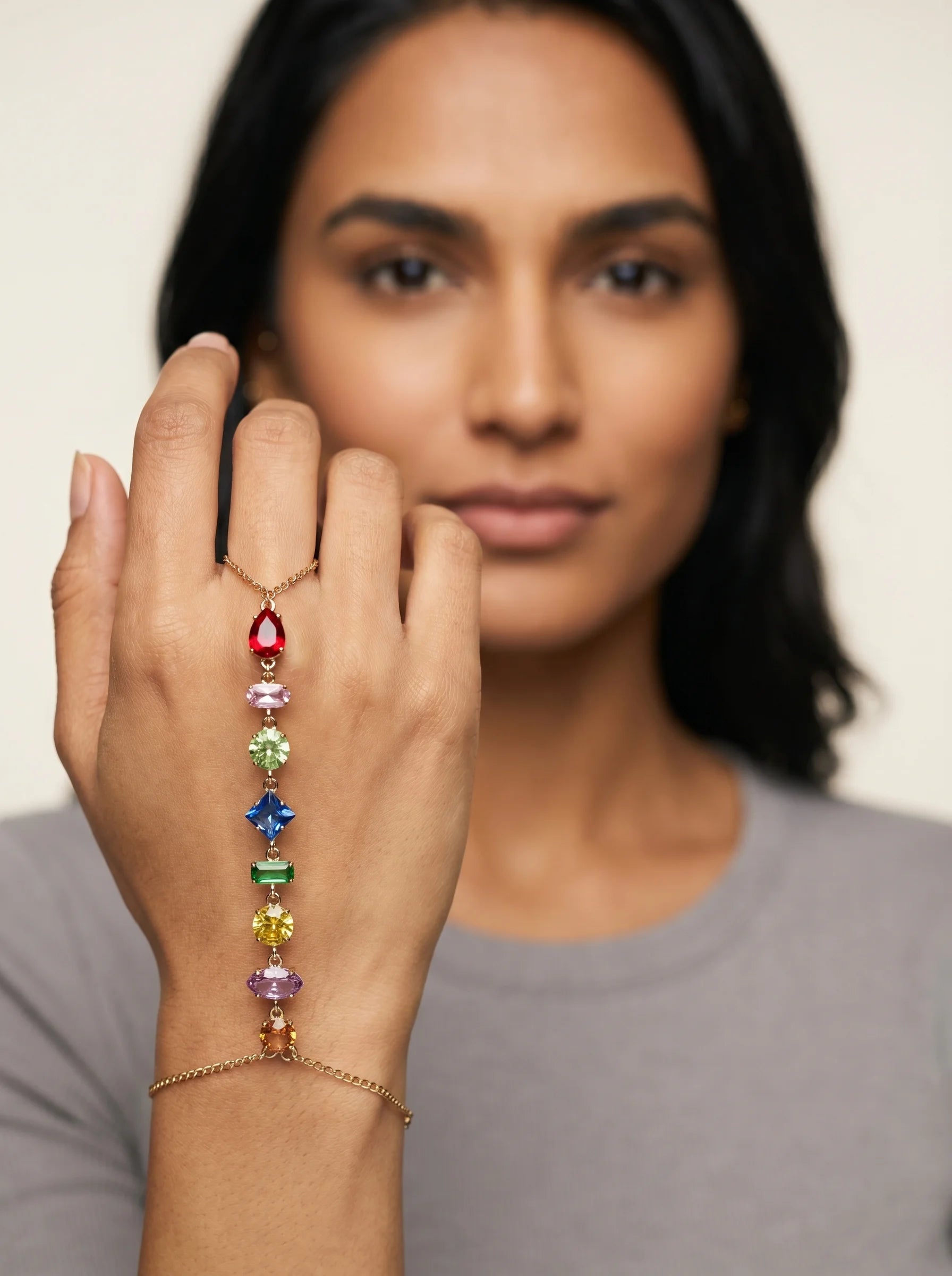Aurum & Isle Prism gold hand harness on model with grey top, hand near face — soft editorial focus.