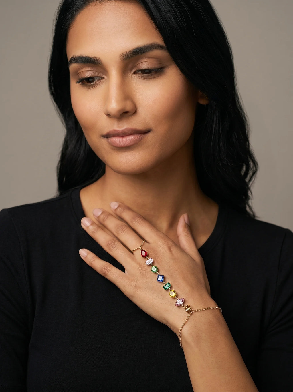 Aurum & Isle Prism hand harness in gold with coloured stones, worn with black top — ring-to-bracelet chain.