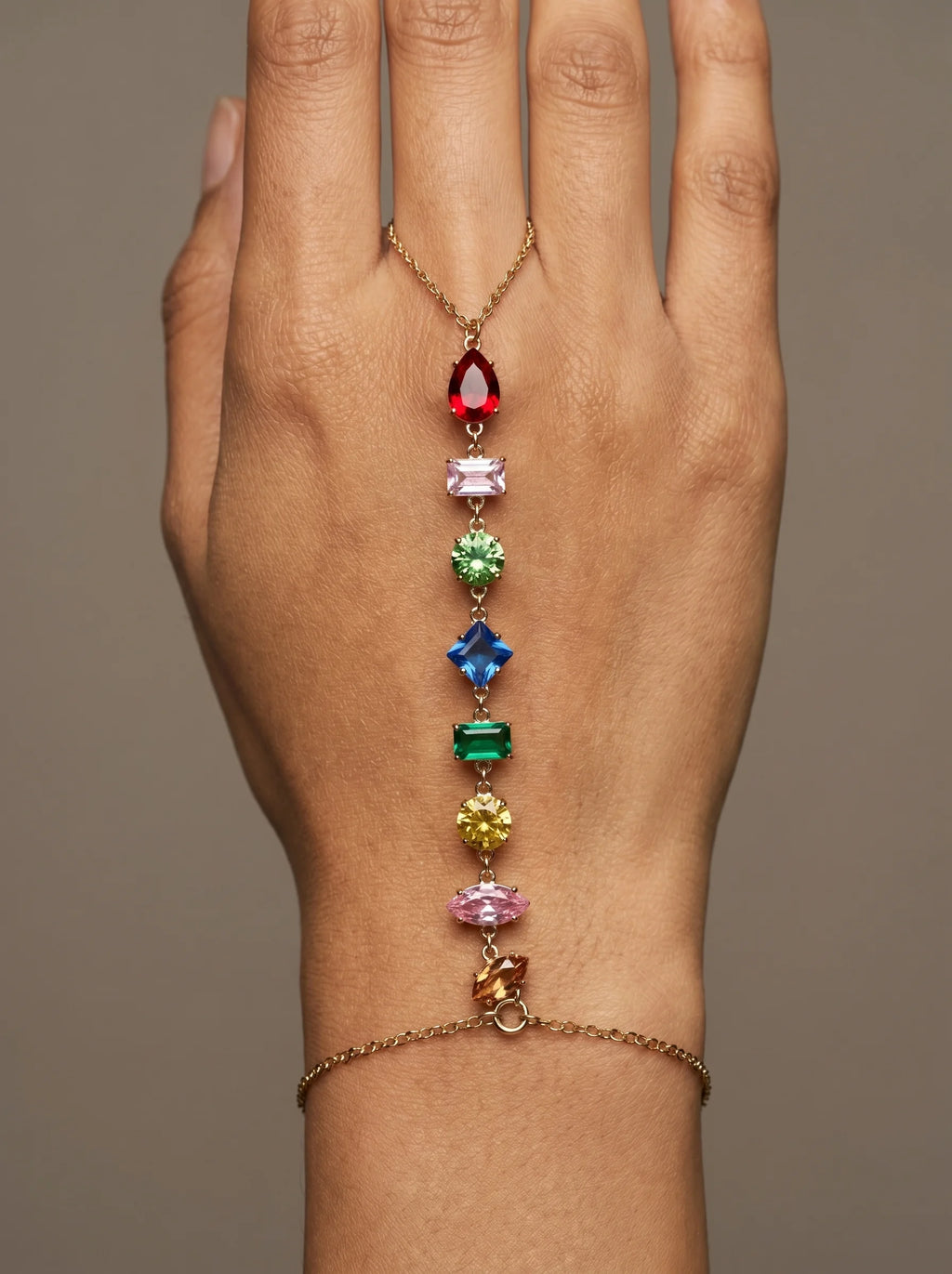Close-up of Aurum & Isle Prism hand harness — gold chain from ring to bracelet with pear, square and round cut stones.