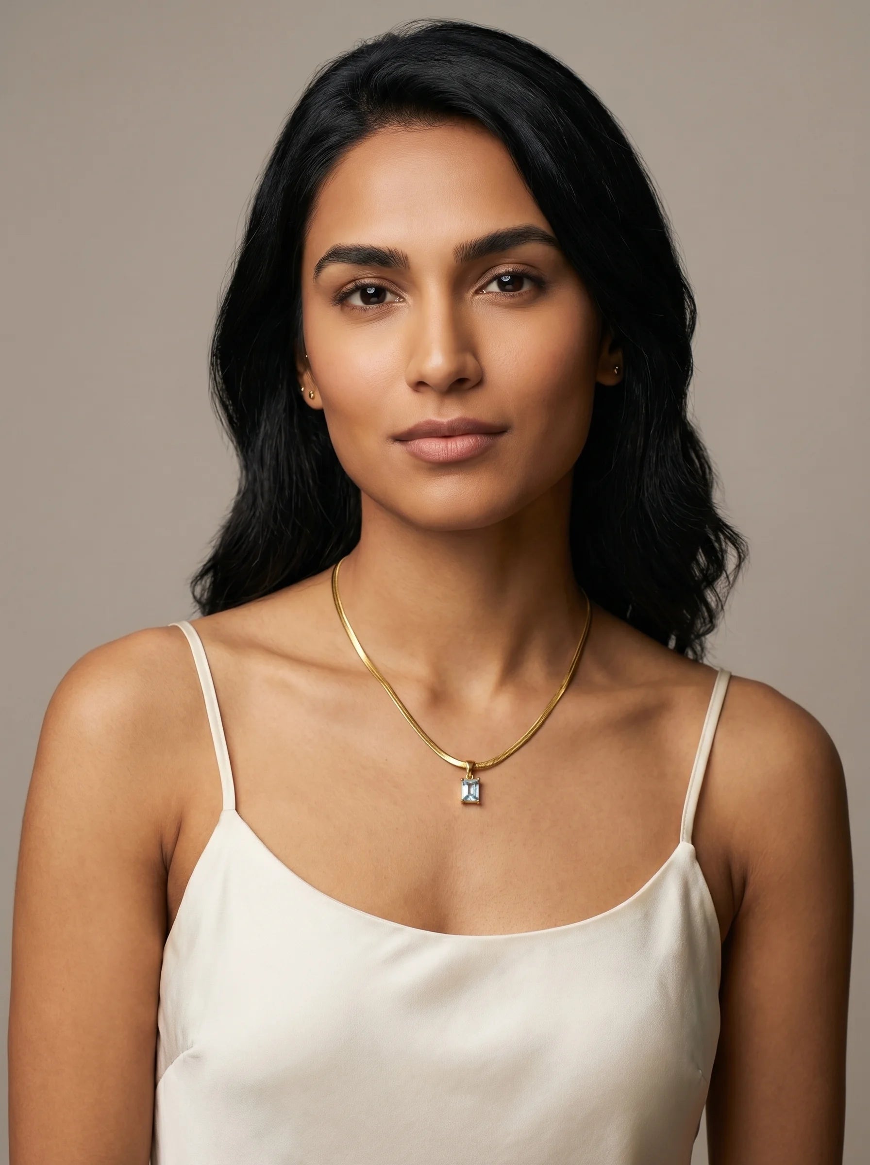 Model wearing Aurum & Isle Soleil gold snake chain with emerald-cut blue pendant, paired with cream slip dress.