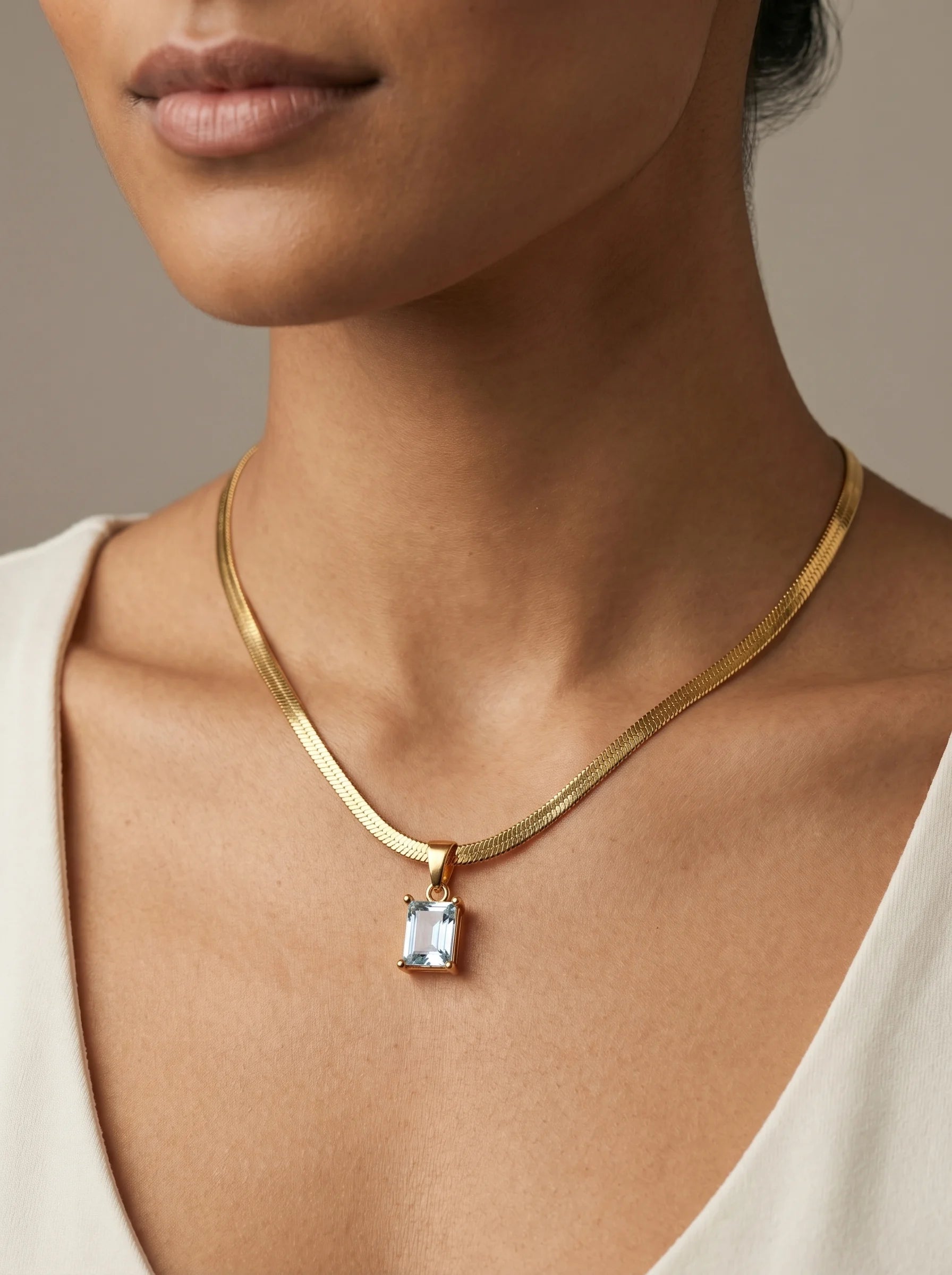 Close-up of Aurum & Isle Soleil herringbone snake chain with emerald-cut blue stone pendant in gold.