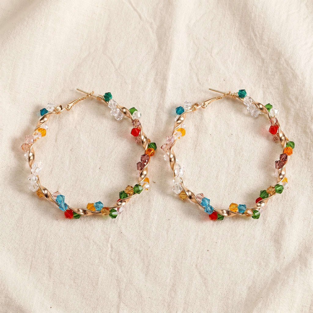 Aria twisted gold hoops wrapped in multicolour bicone crystal beads on cream linen — Aurum & Isle