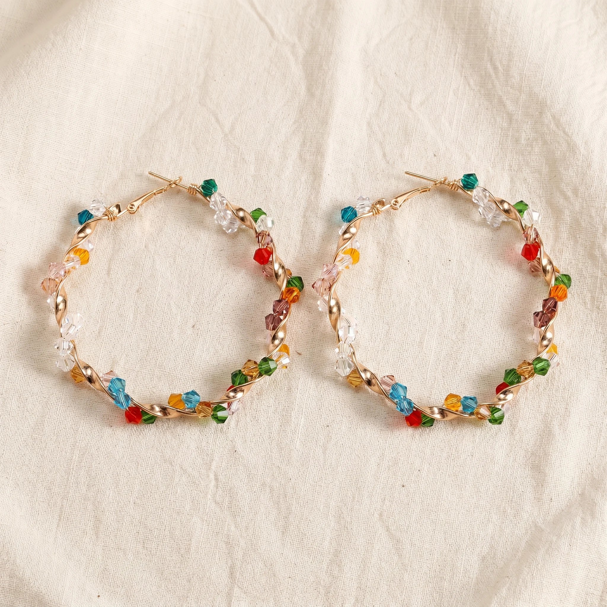 Aria twisted gold hoops wrapped in multicolour bicone crystal beads on cream linen — Aurum & Isle