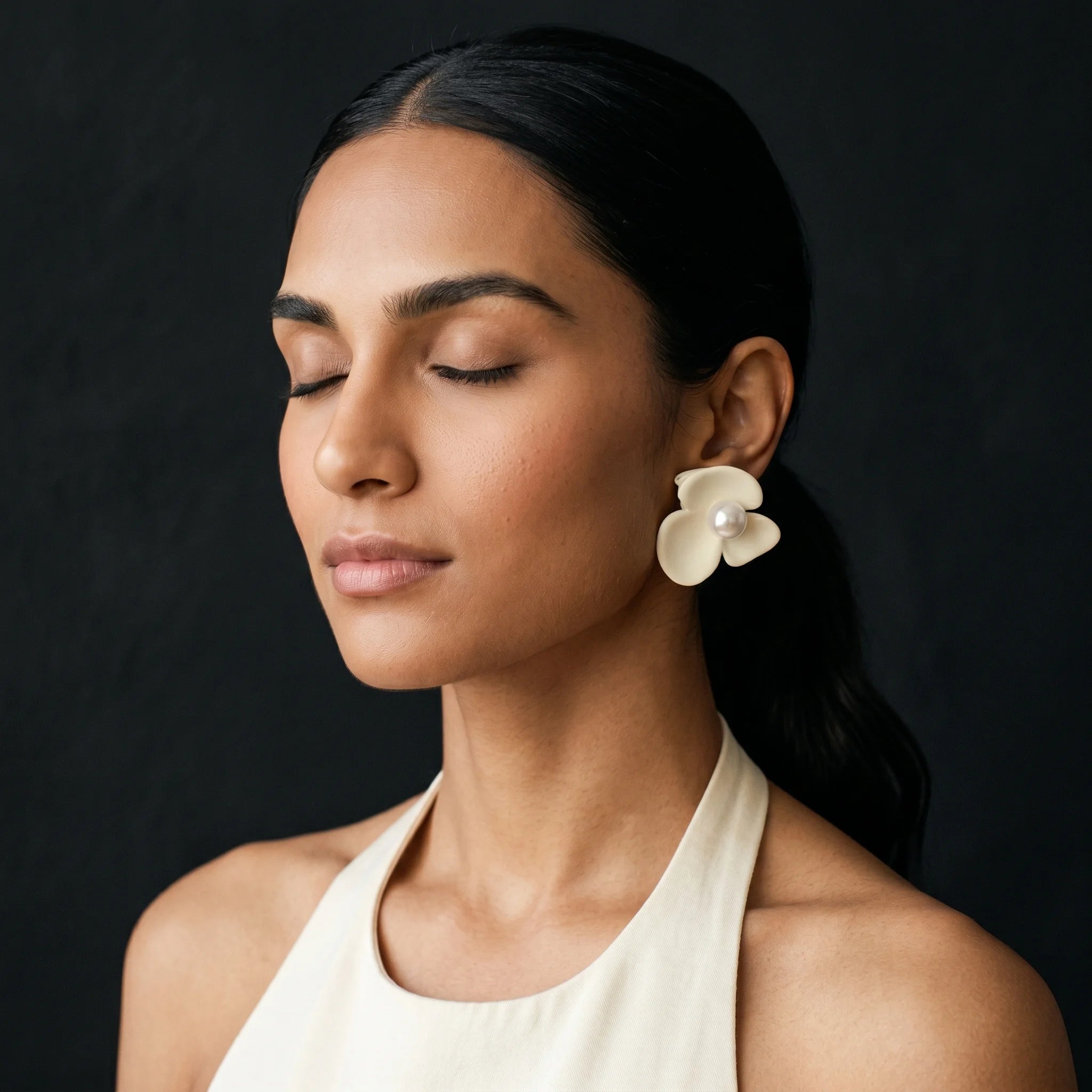 Kalika matte cream flower clip-on earring worn with eyes closed and cream halter — serene profile