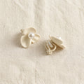 Kalika matte cream flower clip-on earrings showing front face and clip-back closure on cream linen — Aurum & Isle