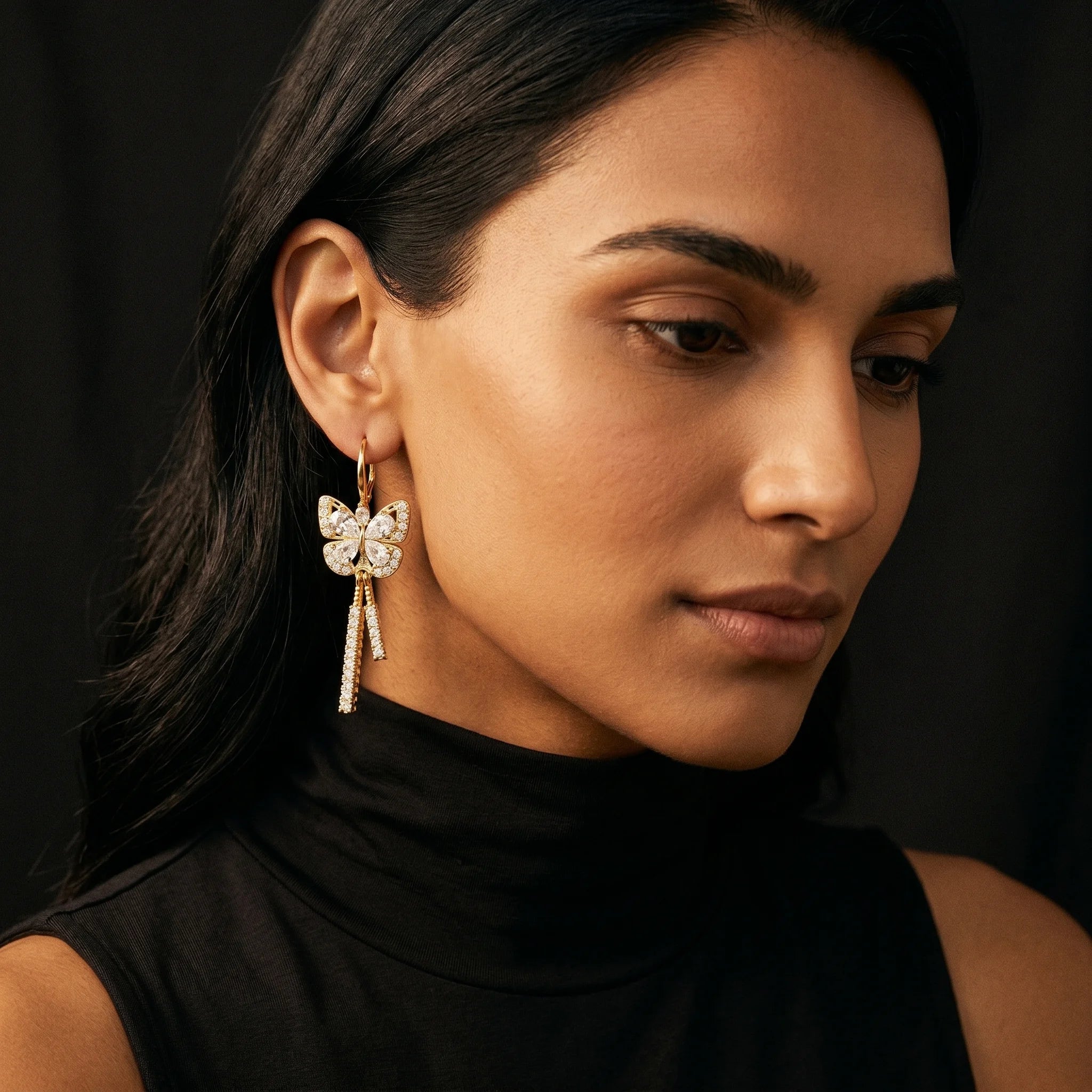 Mira gold butterfly earring with pavé tassel drop worn on model in black turtleneck — close-up