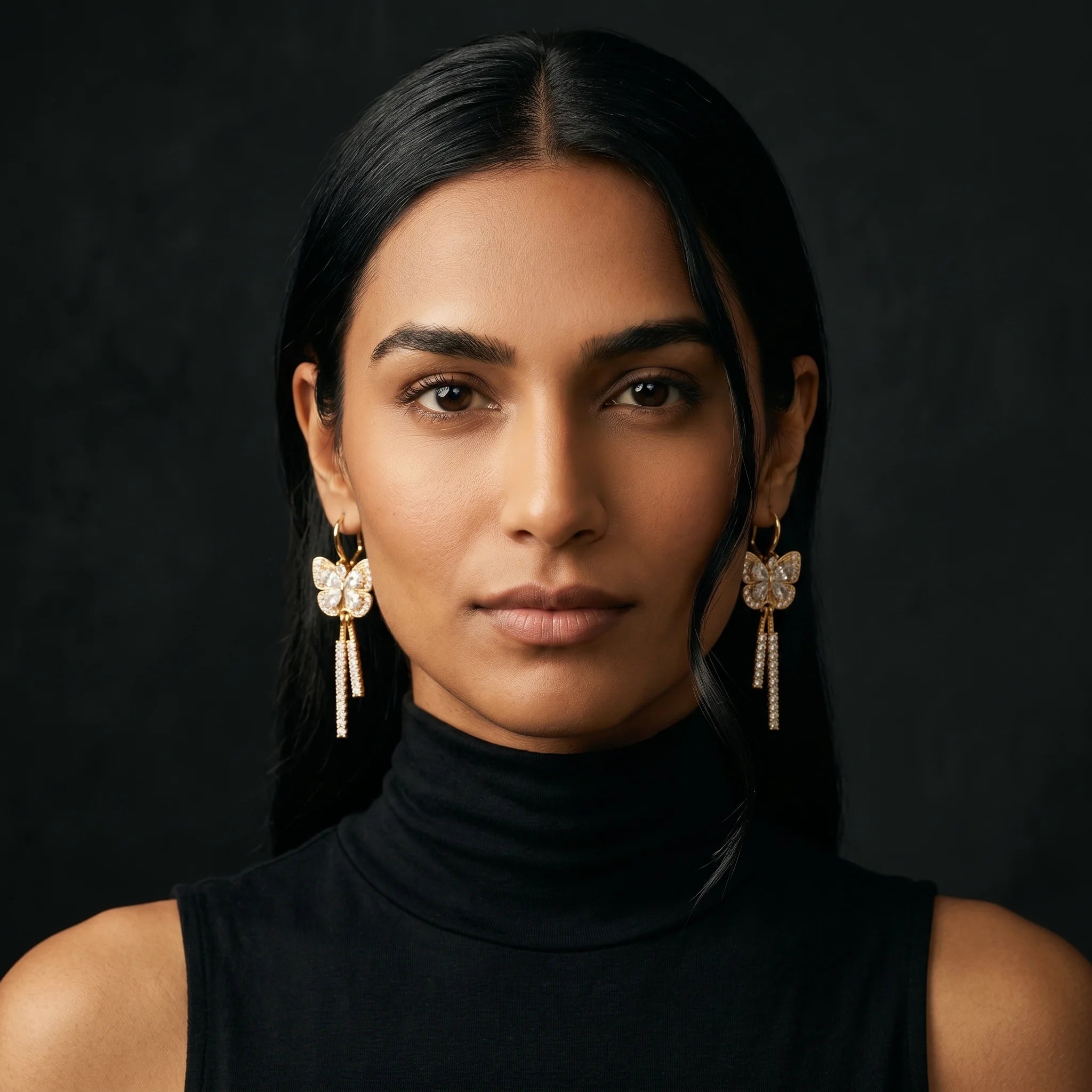 Mira gold butterfly drop earrings worn front-facing with black turtleneck — Aurum & Isle