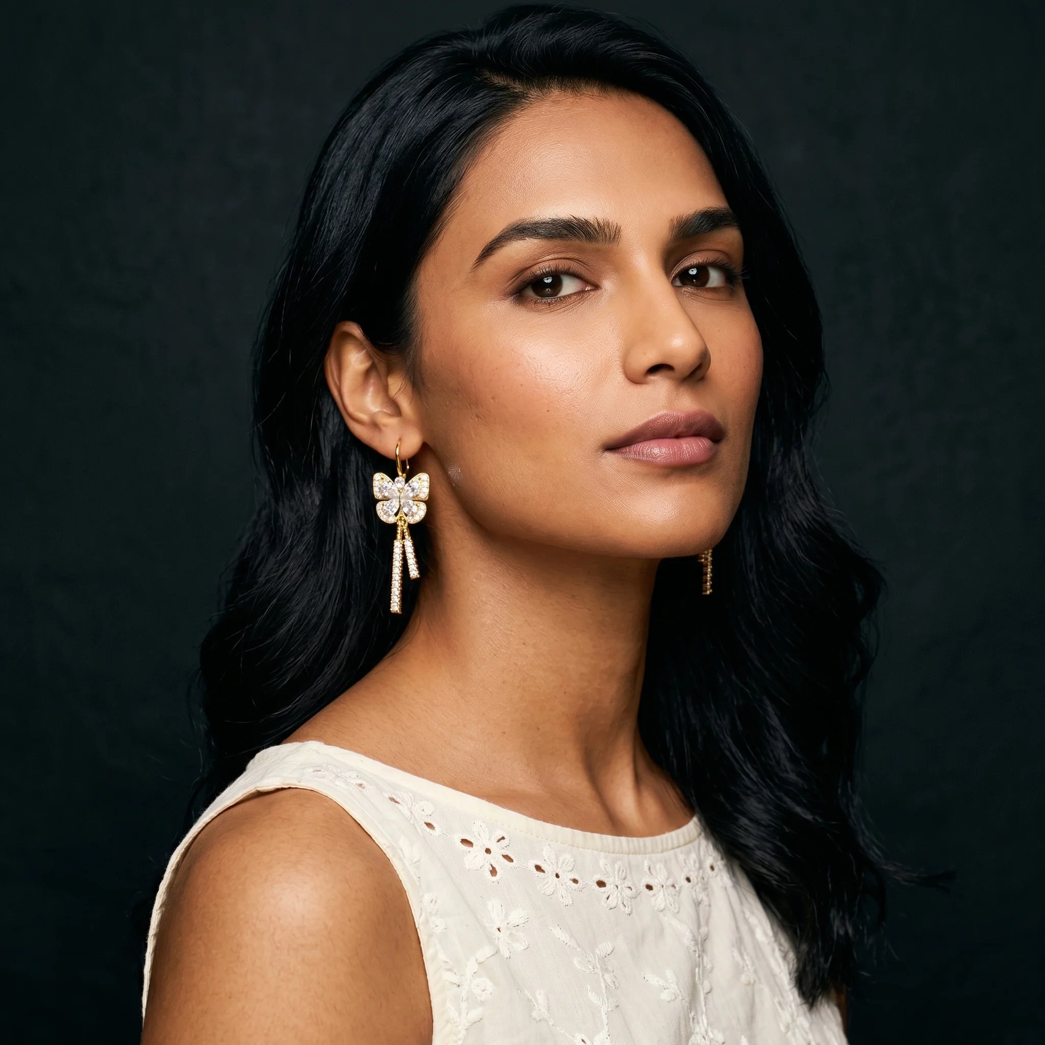 Mira gold butterfly earrings worn with cream eyelet top — soft natural light portrait
