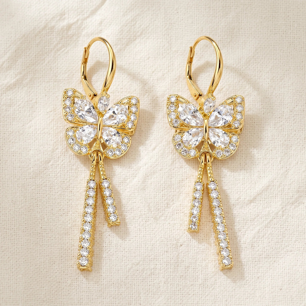 Mira gold butterfly drop earrings with pavé rhinestone wings and tassel drops on cream linen — Aurum & Isle