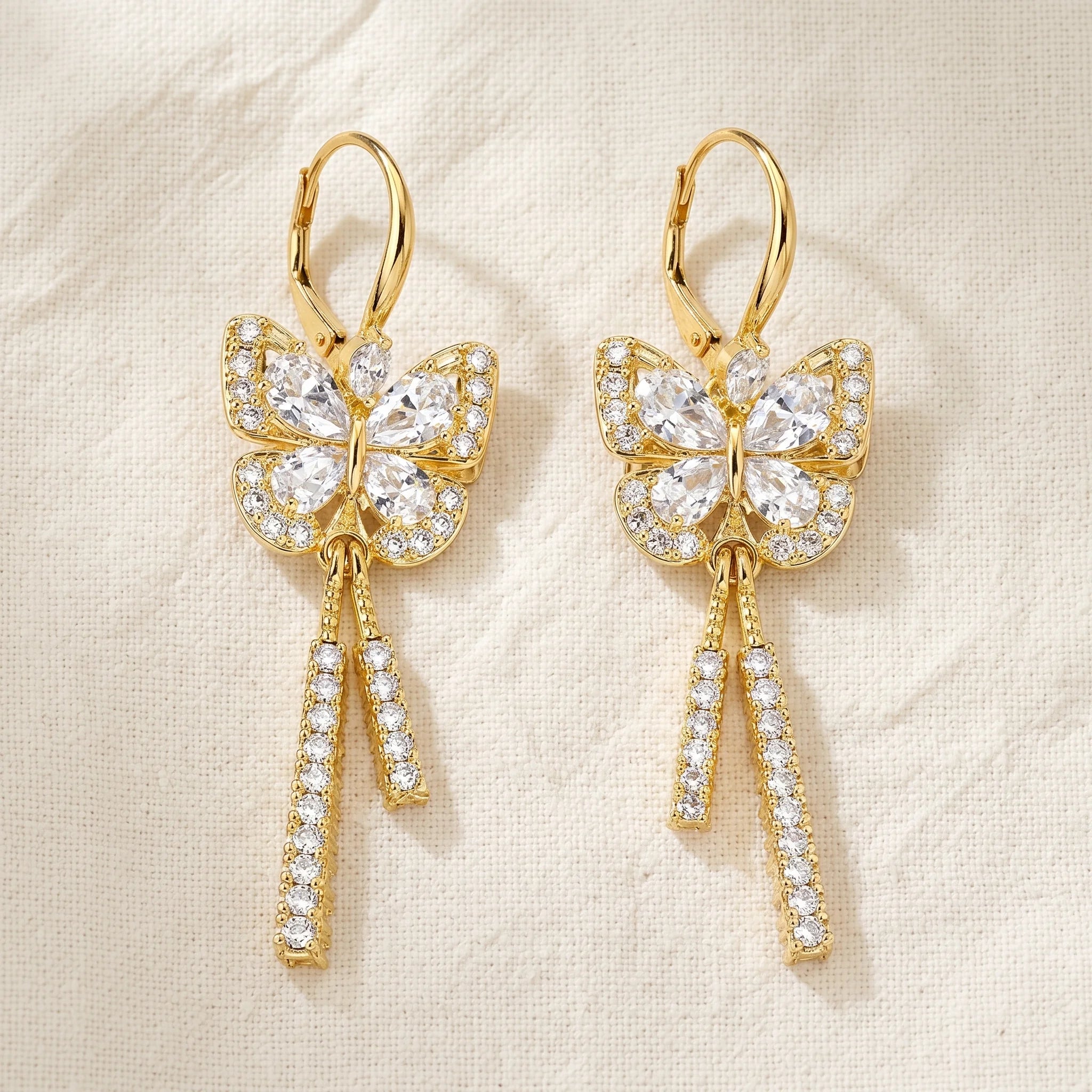 Mira gold butterfly drop earrings with pavé rhinestone wings and tassel drops on cream linen — Aurum & Isle