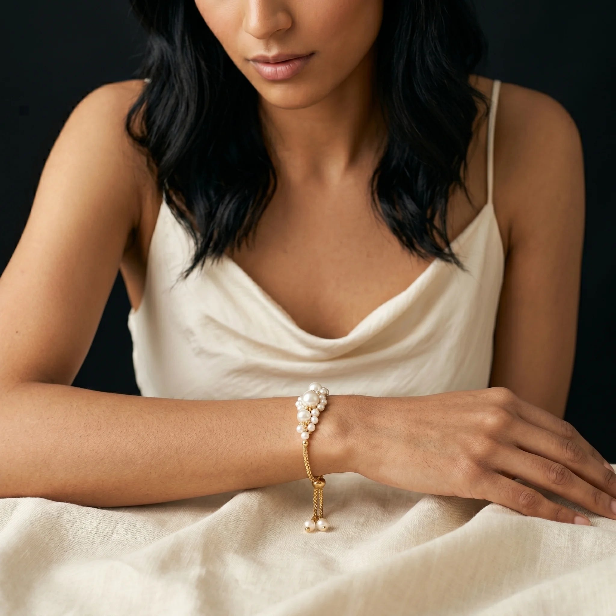 Muktaa imitation pearl cluster bracelet worn on wrist with cream slip dress — close-up