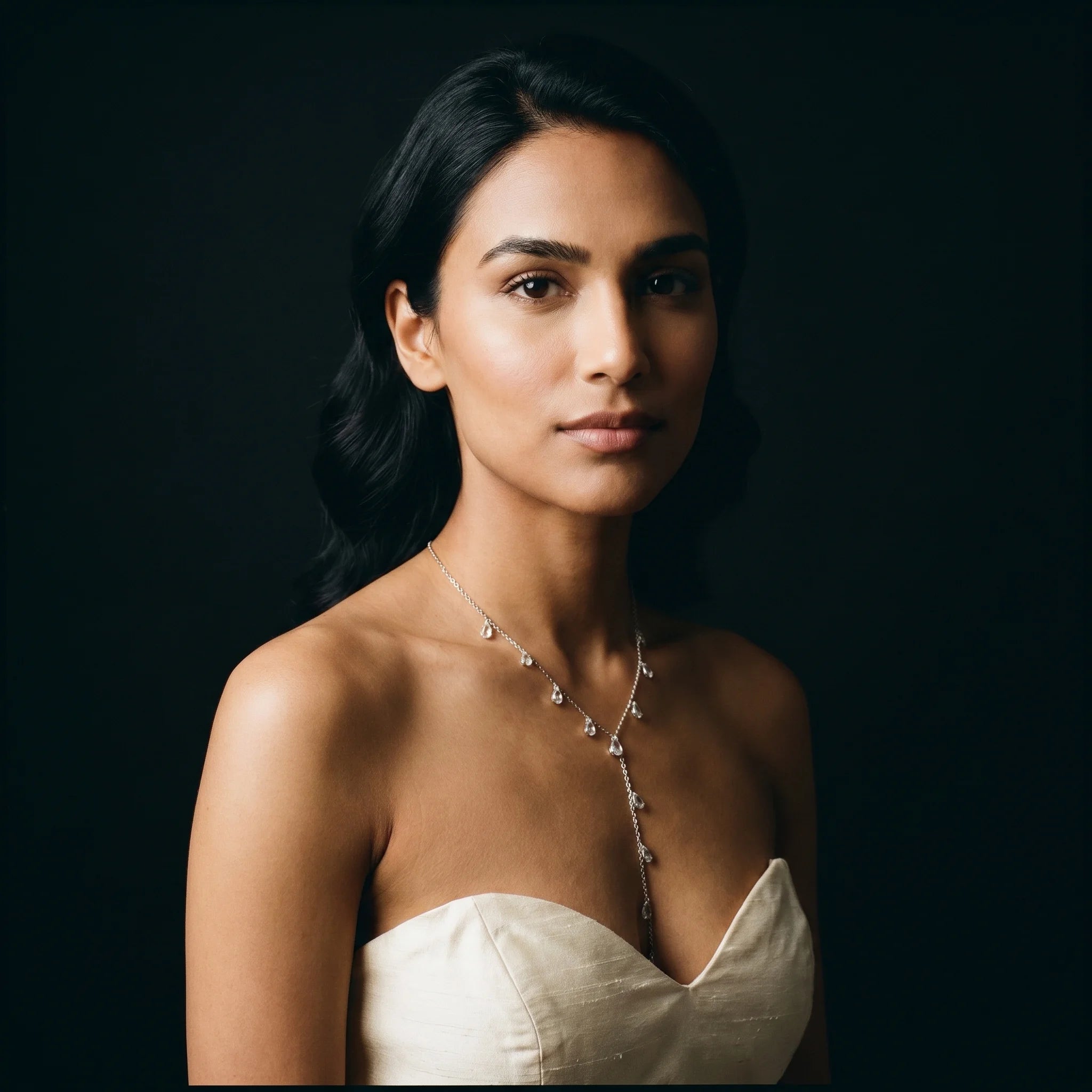 Nira silver CZ Y-necklace worn with cream silk strapless top — soft editorial portrait