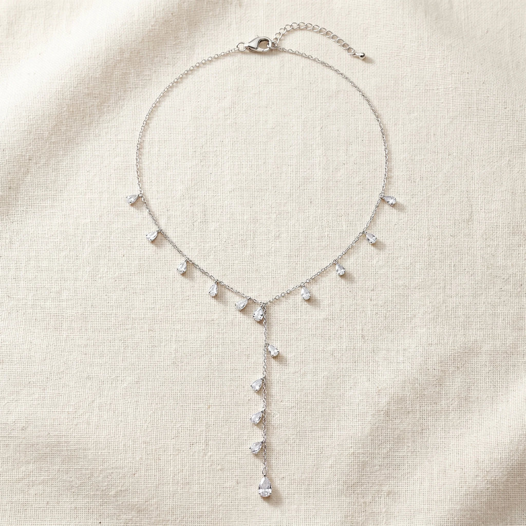 Nira silver Y-necklace with cubic zirconia teardrops and adjustable extender on cream linen — Aurum & Isle