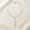 Nira silver Y-necklace with cubic zirconia teardrops and adjustable extender on cream linen — Aurum & Isle