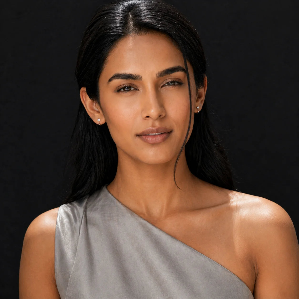 Tara silver CZ solitaire studs worn with grey silk one-shoulder top — front portrait